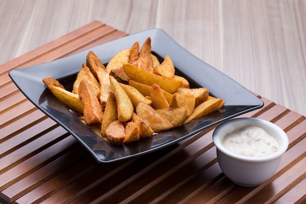 Ciotola di patatine fritte del villaggio e una piccola ciotola di salsa su una tavola di legno