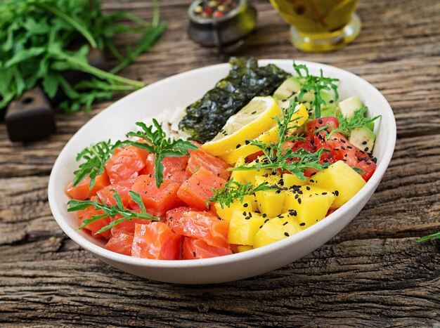 Ciotola di poke di pesce salmone hawaiano con riso, avocado, mango, pomodoro, semi di sesamo e alghe. Ciotola di Buddha. Dieta alimentare.