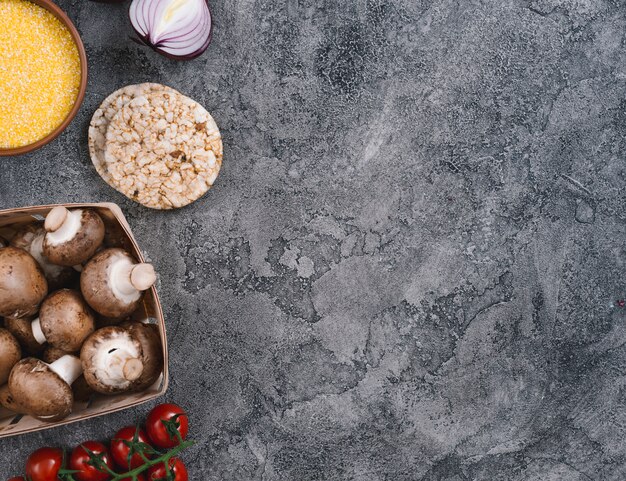 Ciotola di polenta; cipolla; torta di riso soffiato; funghi e pomodorini su sfondo grigio cemento