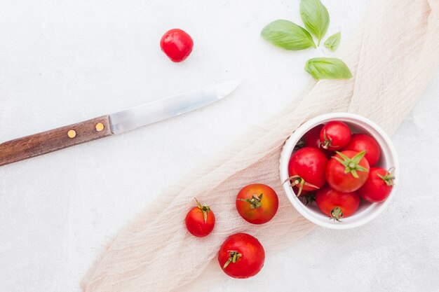 Ciotola di pomodorini rossi con foglie di basilico; sciarpa e coltello affilato