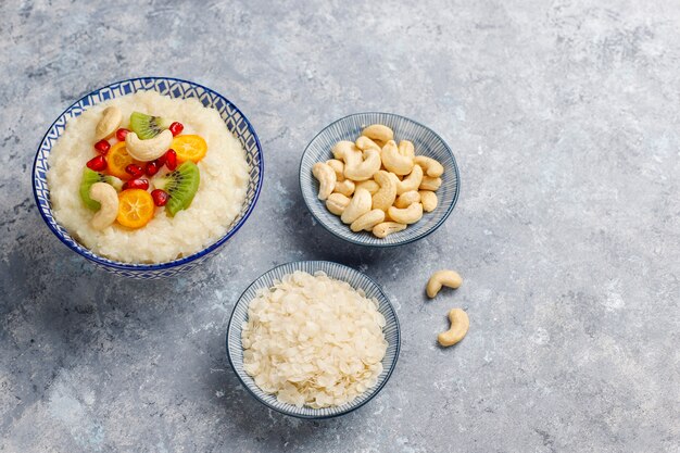 Ciotola di porridge di fiocchi di riso con fette di kiwi, semi di melograno, cumquat e anacardi, vista dall'alto