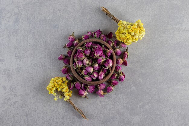 Ciotola di rose in erba e fiori gialli su sfondo di pietra.