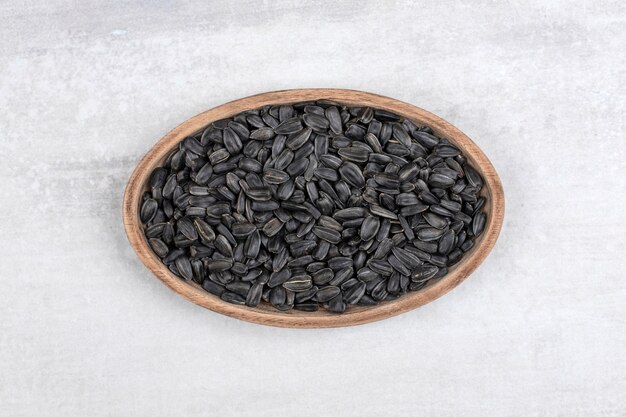 Ciotola piena di semi di girasole neri posti sulla pietra.