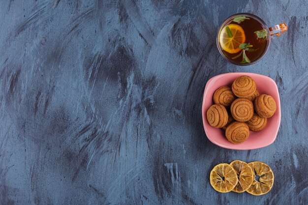 Ciotola rosa di mini torte alla cannella con un bicchiere di tè sulla pietra.