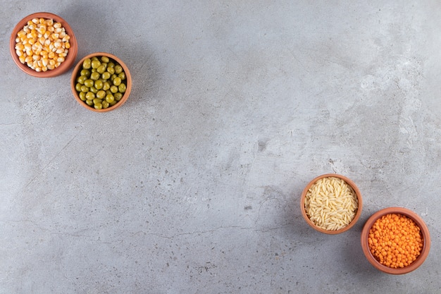 Ciotole di argilla con riso crudo, lenticchie, piselli e semi sul tavolo di pietra.
