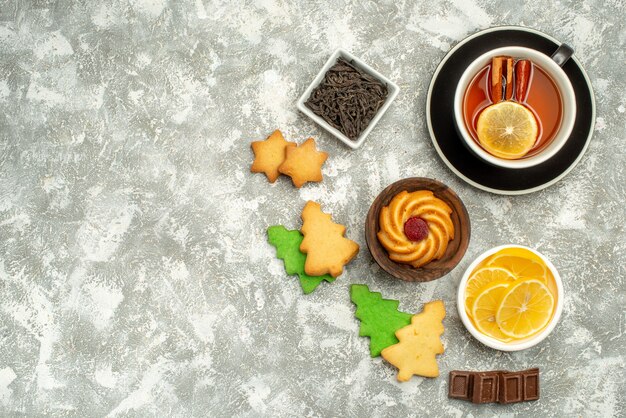 Ciotole di biscotti da tè al limone e cannella con vista dall'alto con fette di limone e cioccolato sulla superficie grigia della copia