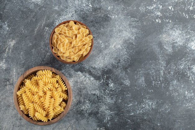 Ciotole di legno piene di fusilli secchi crudi e farfalle tonde.