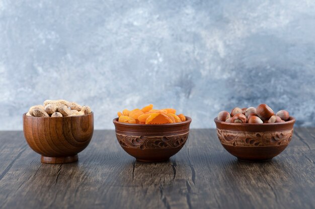 Ciotole di legno piene di noci sane con frutta albicocca secca sulla tavola di legno.