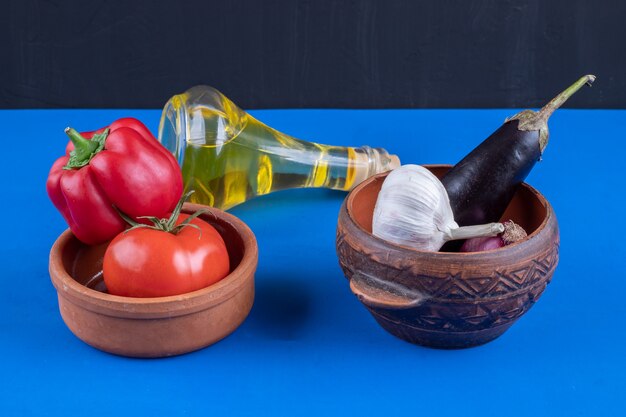 Ciotole di pomodoro, pepe e aglio con olio d'oliva su superficie blu