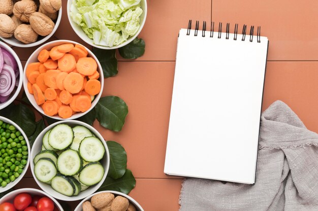 Ciotole di verdure a fette con blocco note e panno