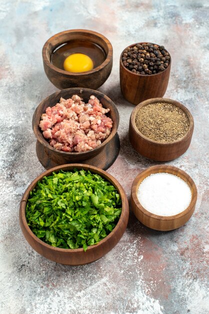Ciotole in fila verticale vista frontale con verdure a base di carne tuorlo d'uovo pepe in polvere pepe nero sale su sfondo nudo