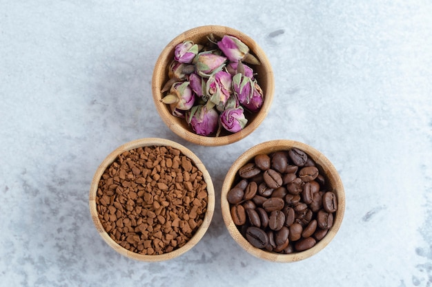 Ciotole in legno piene di chicchi di caffè aromatici, caffè e fiori di rosa appassiti. Foto di alta qualità