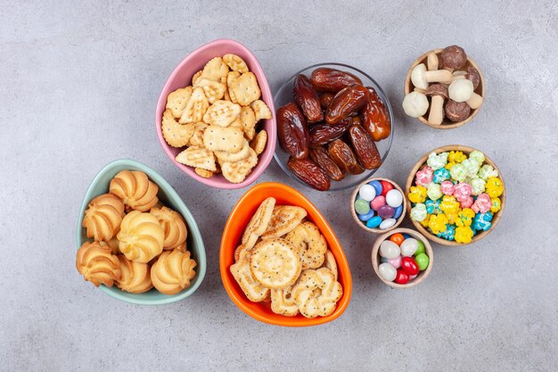 Ciotole piene di caramelle, biscotti, cracker, datteri e funghi al cioccolato su fondo di marmo. Foto di alta qualità