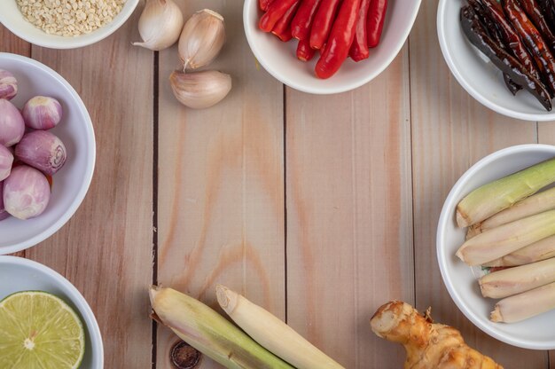 Cipolle rosse, limone, citronella, peperoncino, aglio, galanga e lattuga in una tazza su un pavimento di legno.