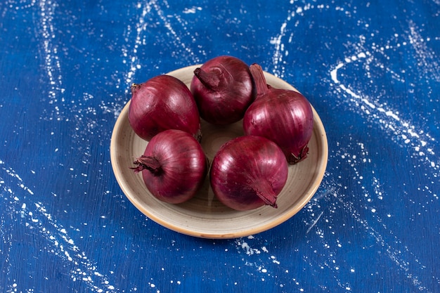 Cipolle rosse mature fresche disposte sul piatto di ceramica