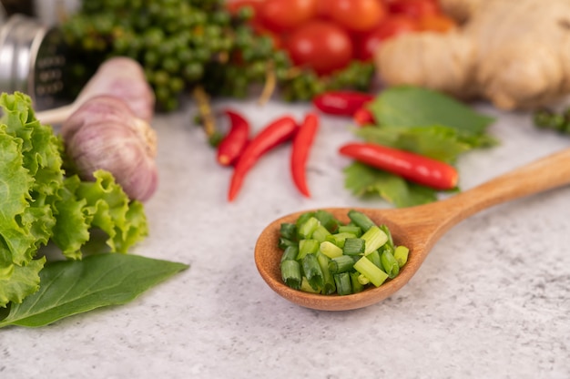 Cipollotto tritato su un cucchiaio di legno con peperoni e pomodori su un pavimento di cemento bianco.