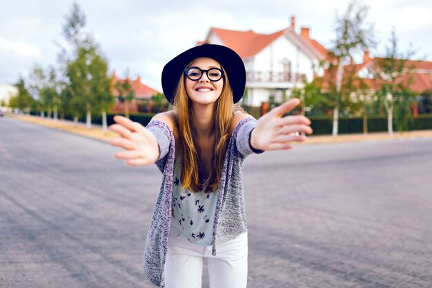 Città autunno moda stile di vita ritratto di giovane donna bionda sensuale, indossa jeans bianchi alla moda, occhiali hipster e cappello, posa in campagna, divertirsi da solo, colori morbidi del film.