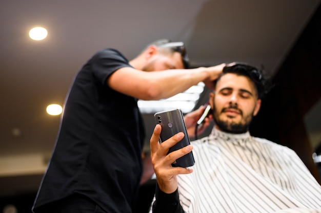 Cliente di angolo basso al negozio di barbiere che controlla il suo telefono