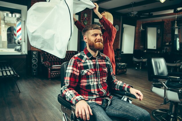 Cliente durante la rasatura della barba nel negozio di barbiere. Barbiere femminile al salone. Parità dei sessi. Donna nella professione maschile.