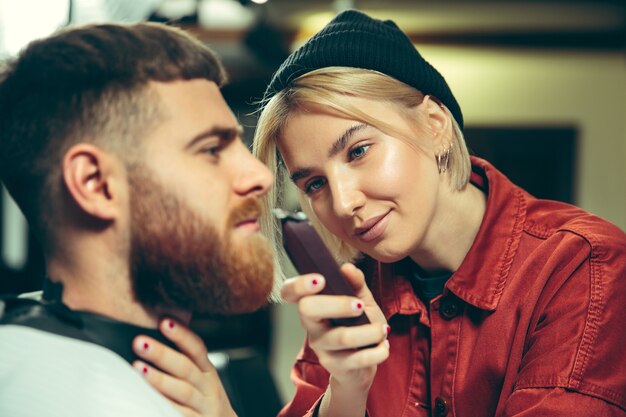 Cliente durante la rasatura della barba nel negozio di barbiere. Barbiere femminile al salone. Parità dei sessi. Donna nella professione maschile.