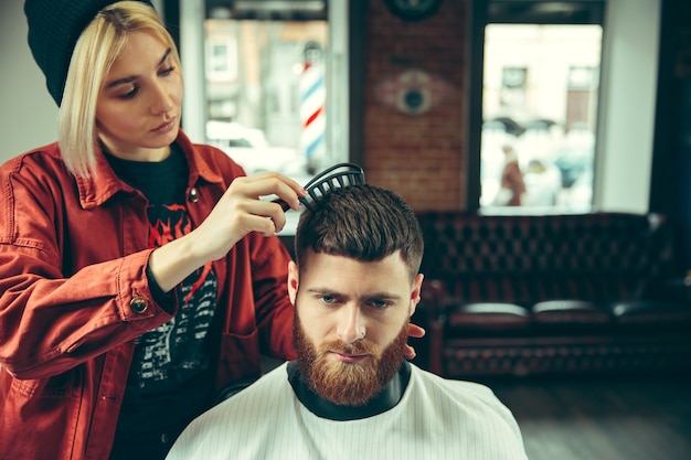 Cliente durante la rasatura della barba nel negozio di barbiere. Barbiere femminile al salone. Parità dei sessi. Donna nella professione maschile.