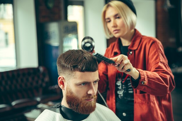 Cliente durante la rasatura della barba nel negozio di barbiere. Barbiere femminile al salone. Parità dei sessi. Donna nella professione maschile.