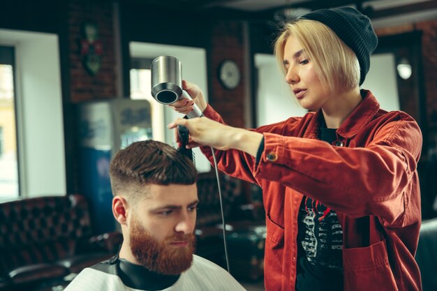 Cliente durante la rasatura della barba nel negozio di barbiere. Barbiere femminile al salone. Parità dei sessi. Donna nella professione maschile.