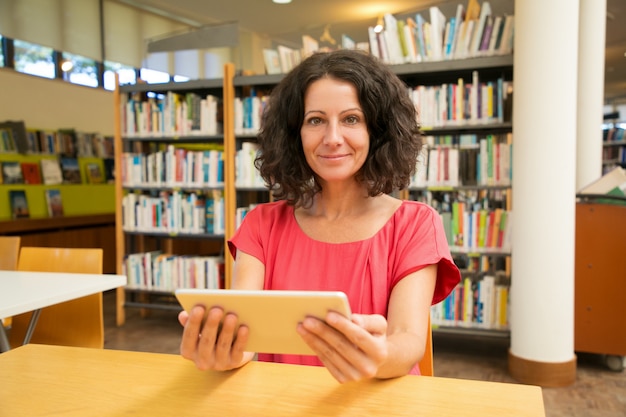 Cliente femminile soddisfatto con l'aggeggio che posa nella biblioteca pubblica