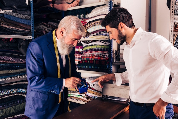 Cliente maschio che seleziona la bobina del filo con lo stilista maschio nel suo negozio