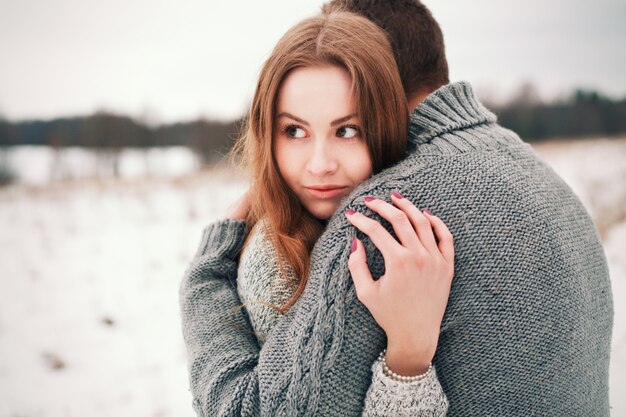 Close-up della donna bionda abbraccia il suo ragazzo nel prato innevato