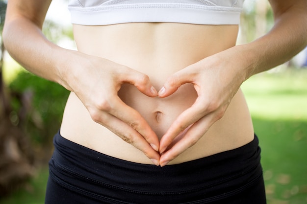 Close-up delle mani femminili che modellano cuore sul ventre