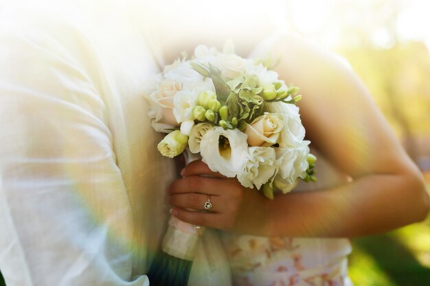 Close-up di bouquet di nozze bianche in mani di sposa abbraccia sposo