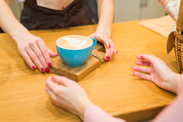 Close-up di cameriera dando tazza di caffè con schiuma di latte art al cliente sul tavolo di legno