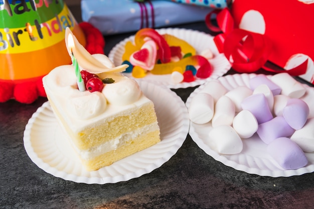 Close-up di fetta torta; marshmallow e caramelle sul piatto di carta