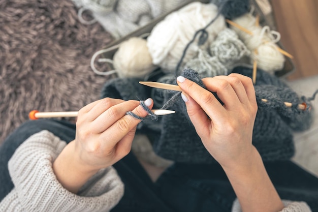 Close-up di mani femminili che magliano un maglione di lana grigia vista superiore