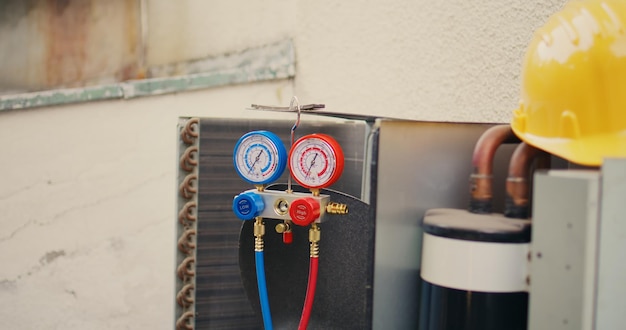 Close up di misuratori di collettore utilizzati per il controllo del refrigerante del condizionatore d'aria che ha bisogno di manutenzione e casco di protezione.