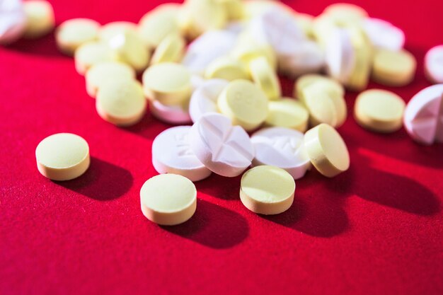 Close-up di pillole bianche e gialle su sfondo rosso