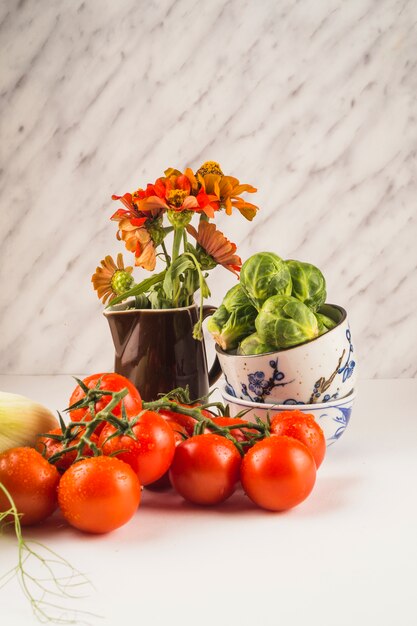 Close-up di pomodori rossi freschi; cavoletti di Bruxelles e fiori sul ripiano del tavolo bianco