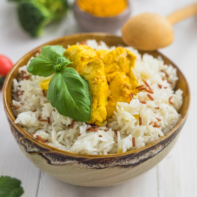 Close-up di riso bollito fresco; foglie di basilico e pollo fritto in una ciotola con un cucchiaio di legno