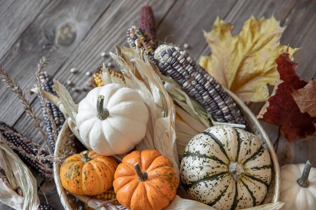 Close-up di zucca, mais e foglie di autunno su uno sfondo di legno, in stile rustico.