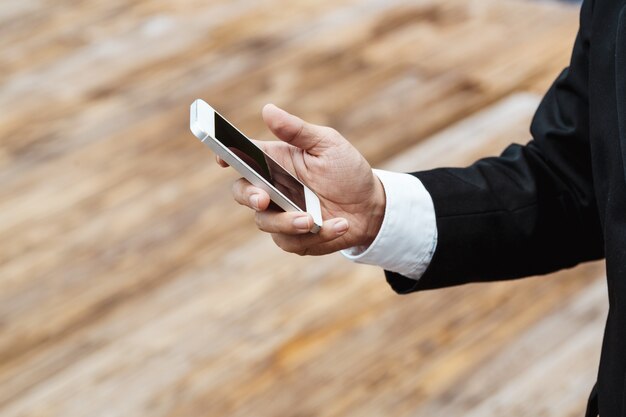 Close-up elegante uomo d&#39;affari che indossa abito nero moderno e camicia bianca e texting sul telefono cellulare intelligente