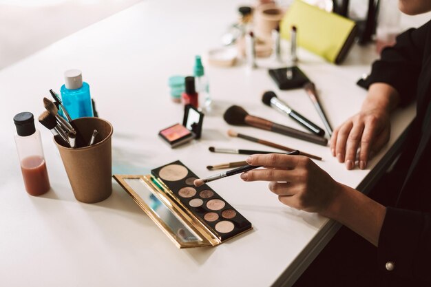 Close up make up artist seduto alla scrivania con una varietà di prodotti cosmetici isolati