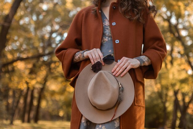 Close-up mani dettagli di attraente donna alla moda che tiene cappello e occhiali da sole a piedi nel parco vestito con caldo cappotto autunno alla moda street fashion style accessori