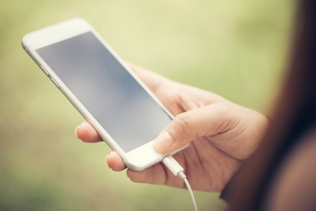 Close-up mano toccare sul telefono cellulare bianco vuoto schermo concetto di stile di vita all&#39;aperto sullo sfondo sfocato della natura - può essere utilizzato immagine imbrattata. Immagini di stile d&#39;effetto vintage.