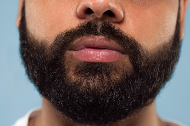 Close up ritratto del volto di giovane uomo indù con barba e labbra su sfondo blu. Sembra calmo. Emozioni umane, espressione facciale, concetto di pubblicità. Spazio negativo.