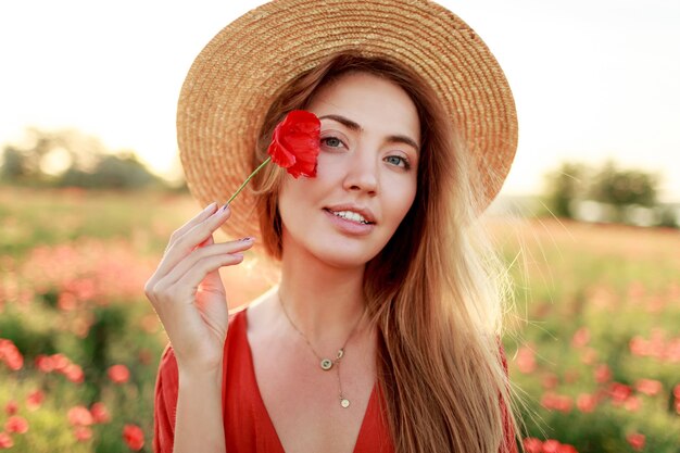Close up ritratto di bella giovane donna romantica con il fiore di papavero in mano in posa sul fondo del campo. Indossare un cappello di paglia. Colori tenui.