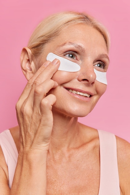 Close up ritratto di donna di mezza età applica cerotti di bellezza sotto gli occhi