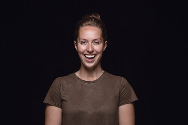 Close up ritratto di giovane donna isolata su nero di sfondo per studio. Photoshot di vere emozioni del modello femminile. Sorridere, sentirsi pazzi felici, ridere. Espressione facciale, concetto di emozioni umane.