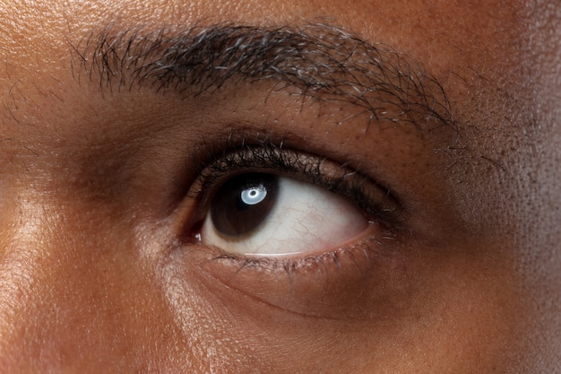 Close up ritratto di giovane uomo afro-americano sulla parete blu. Emozioni umane, espressione facciale, annuncio, vendite o concetto di bellezza. servizio fotografico di un occhio. Sembra calmo, guardando in alto.