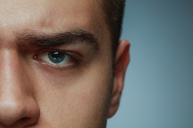 Close-up ritratto di giovane uomo isolato su grigio di sfondo per studio. Il viso e l'occhio azzurro del modello maschio caucasico. Concetto di salute e bellezza maschile, cura di sé, cura del corpo e della pelle, medicina o fisiologia.